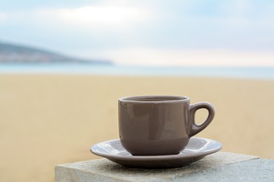 Photo of Ceramic cup of hot drink on stone surface near sea in morning, space for text