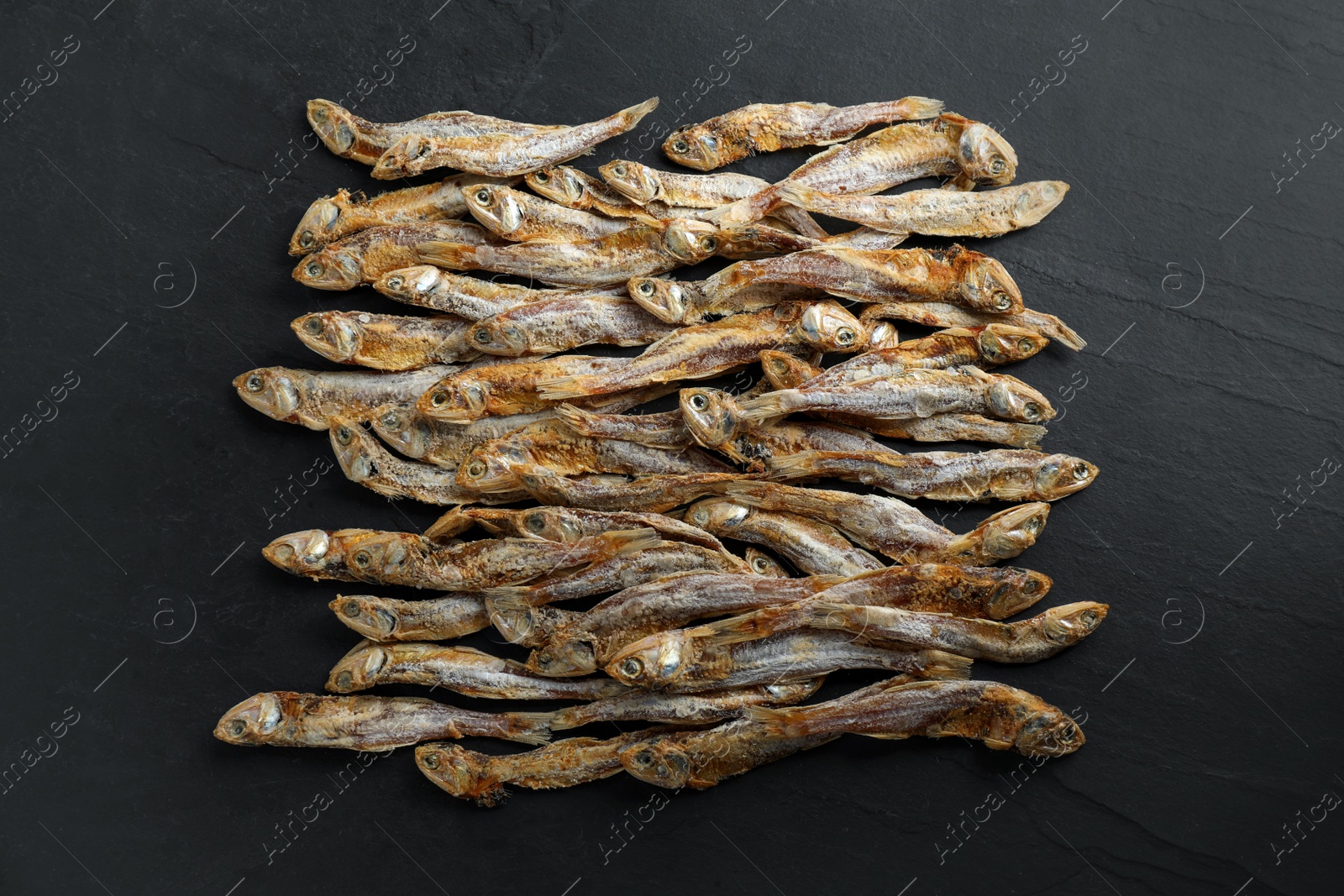 Photo of Delicious dried anchovies on black table, flat lay