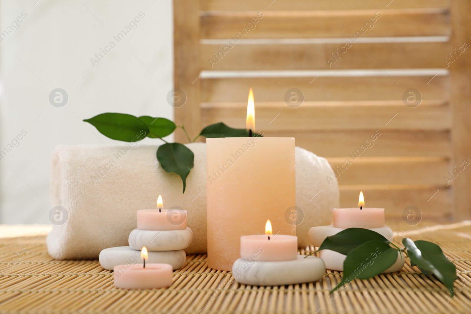 Photo of Composition of spa stones, towel and burning candles on bamboo mat