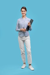 Happy secretary with clipboard and pen on light blue background