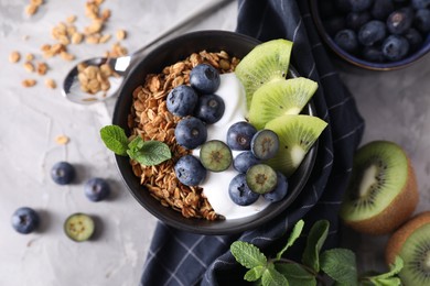 Photo of Tasty granola with yogurt, blueberries and kiwi in bowl on gray textured table, flat lay