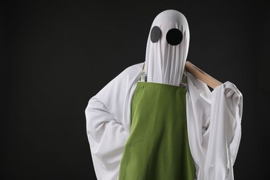 Photo of Woman in ghost costume and apron with rolling pin on black background, space for text