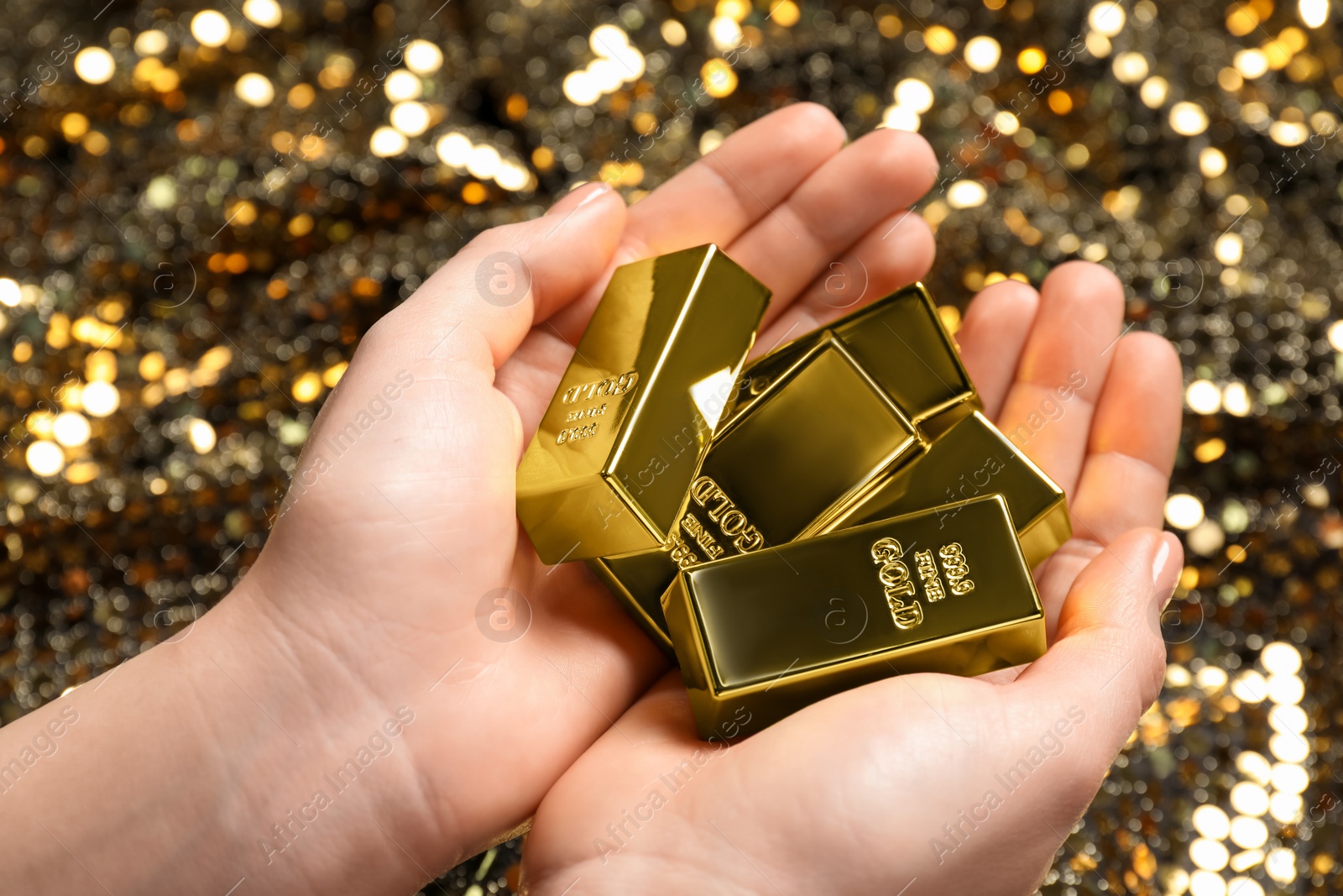 Photo of Woman holding shiny gold bars against sequin fabric, closeup