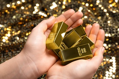 Woman holding shiny gold bars against sequin fabric, closeup