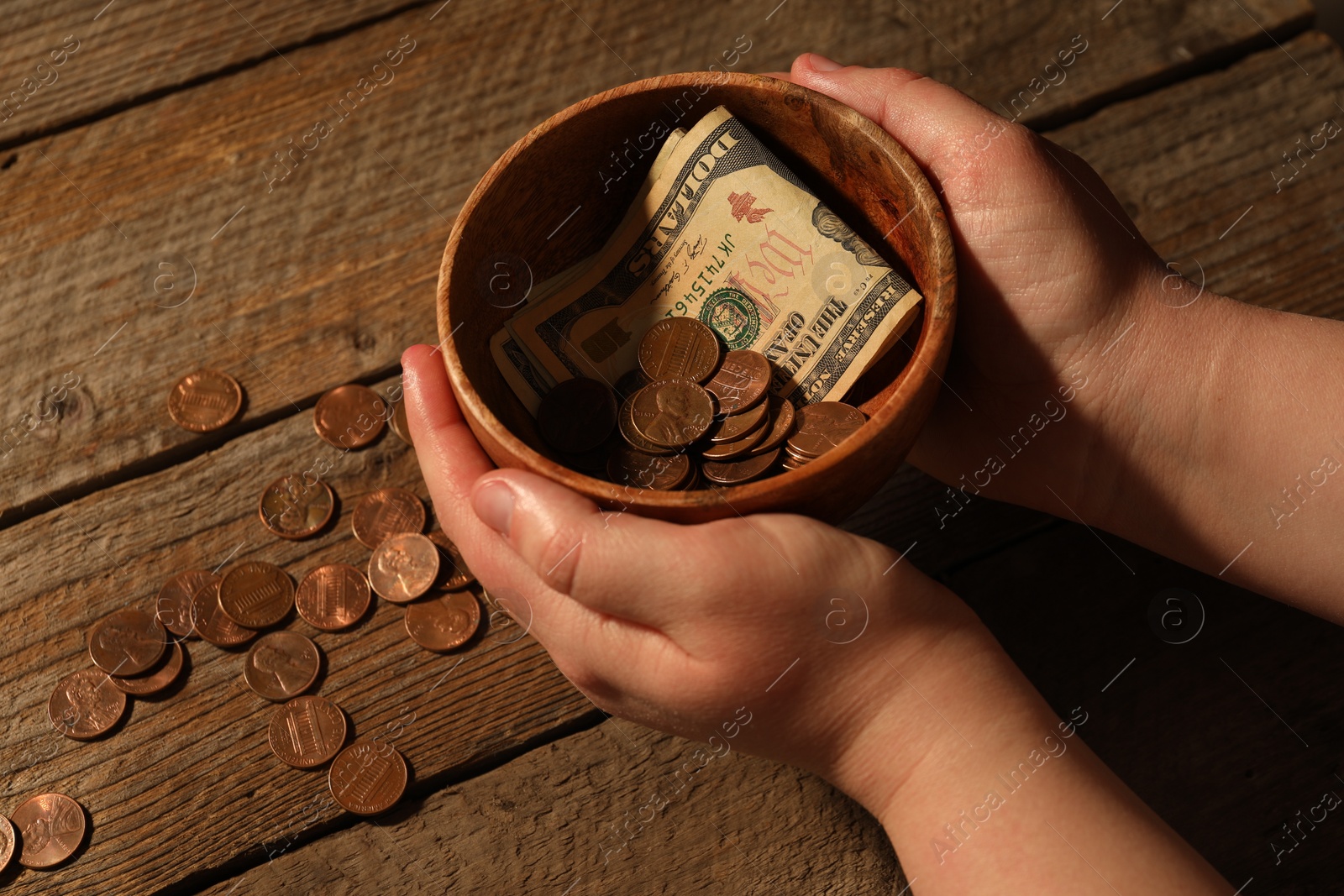 Photo of Donate and give concept. Woman holding bowl with coins and dollar banknotes at wooden table, closeup