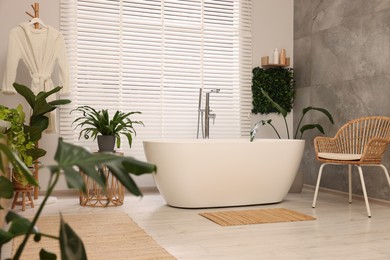 Green artificial plants, robe and tub in bathroom