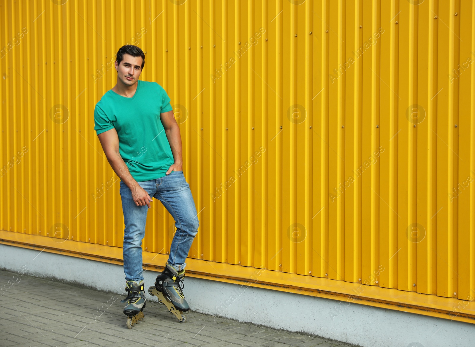 Photo of Handsome young man with inline roller skates standing near yellow building, space for text