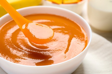 Photo of Spoon of healthy baby food over bowl, closeup