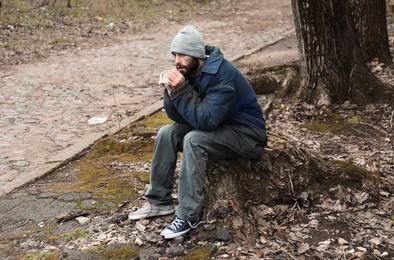 Poor homeless man sitting on stump outdoors