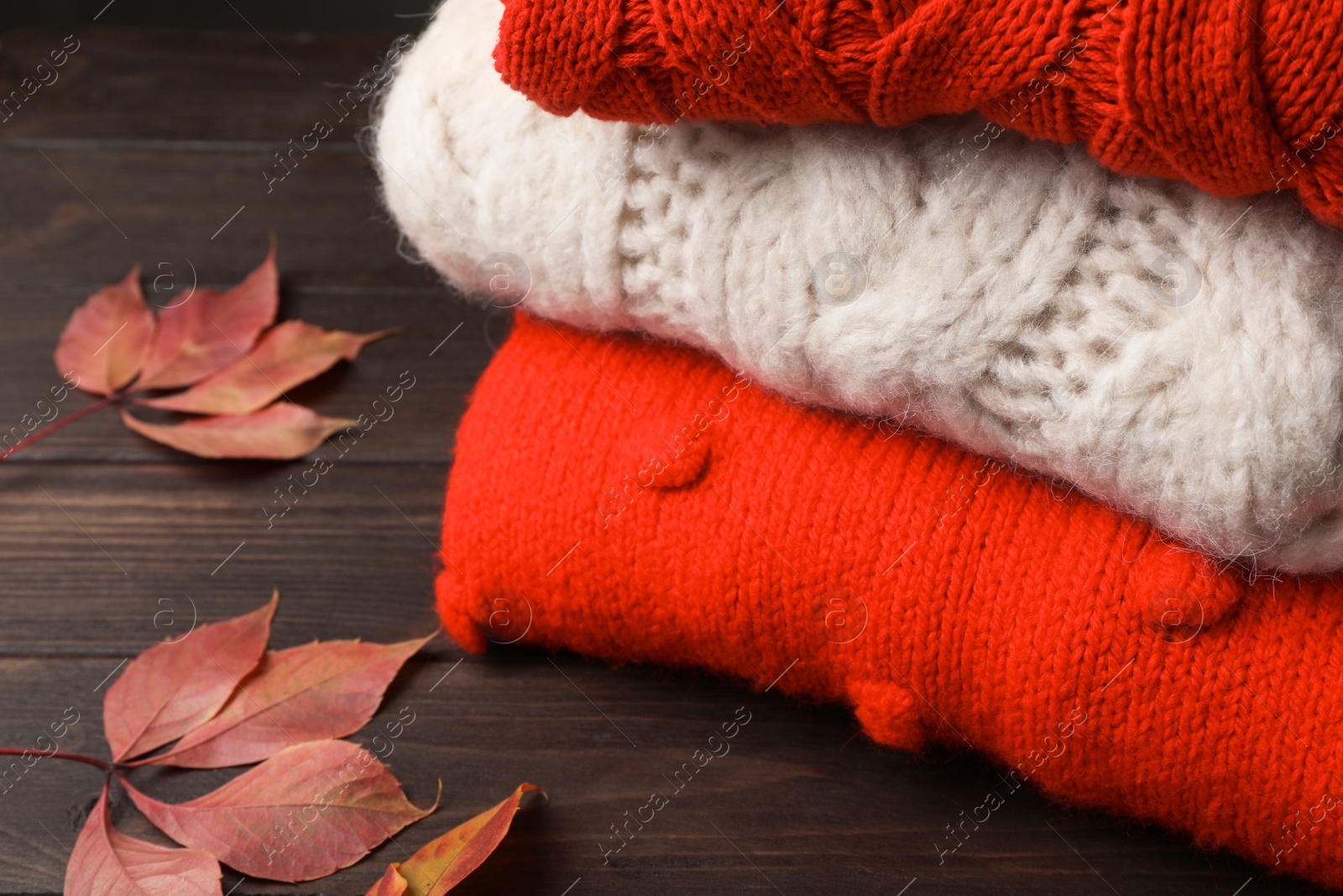 Photo of Stack of folded knitted sweaters and autumn leaves on table, closeup. Space for text