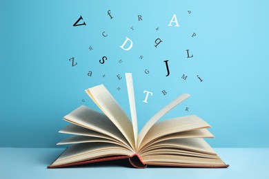 Image of Open book with letters flying out of it on light blue background