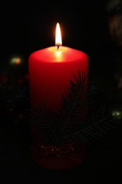 Photo of Red burning candle and fir tree branch in darkness, closeup view
