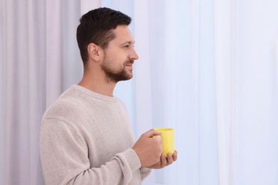 Man holding yellow ceramic mug at home. Space for text