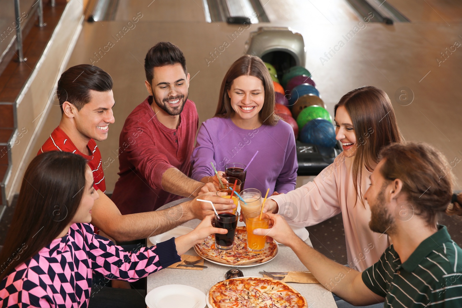 Photo of Group of friends with drinks and pizza in bowling club