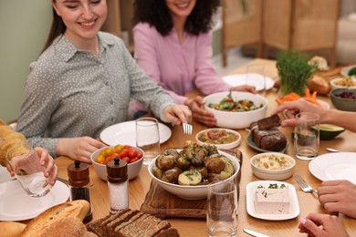 Photo of Friends eating vegetarian food at wooden table indoors, closeup