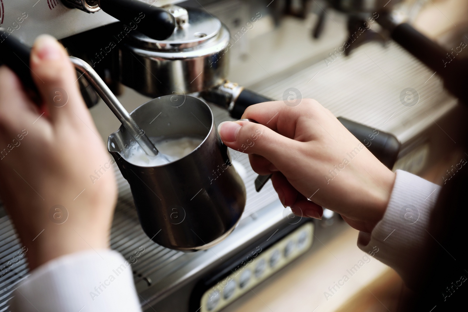 Photo of Barista steaming milk using modern coffee machine, closeup