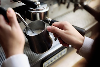 Barista steaming milk using modern coffee machine, closeup