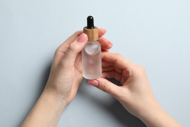 Woman holding bottle with serum on light blue background, closeup