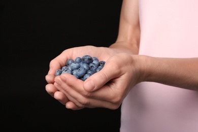 Photo of Woman holding juicy fresh blueberries on black background, closeup