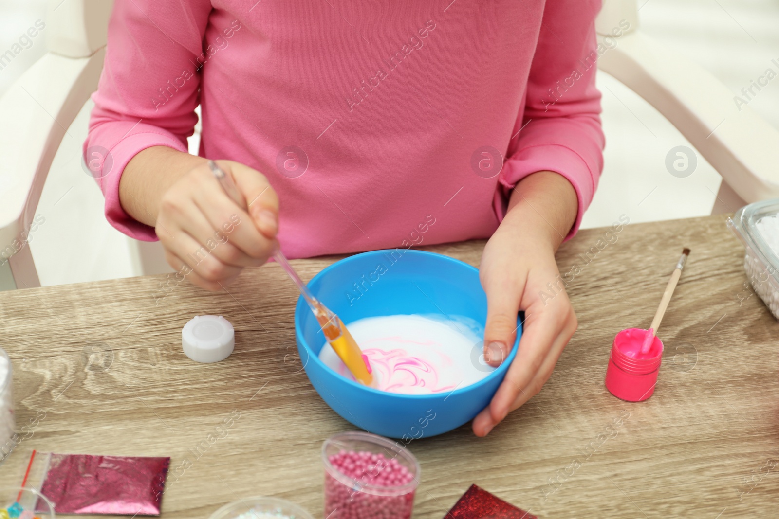 Photo of Little girl mixing ingredients with silicone spatula at table, closeup. DIY slime toy