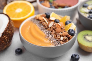 Photo of Bowl of delicious fruit smoothie with fresh orange slices, blueberries and granola on white table, closeup