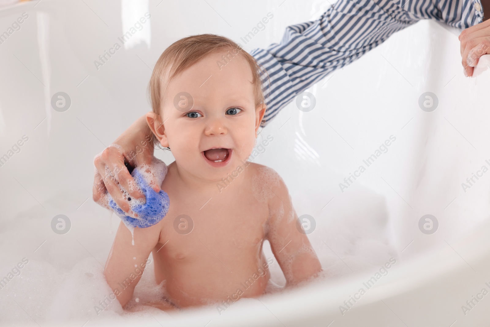 Photo of Mother washing her little baby with sponge in tub at home, closeup