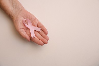 Senior woman holding pink ribbon on light background, top view with space for text. Breast cancer awareness