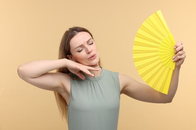 Photo of Beautiful woman waving yellow hand fan to cool herself on beige background