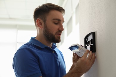 Photo of Man installing home security system on white wall in room