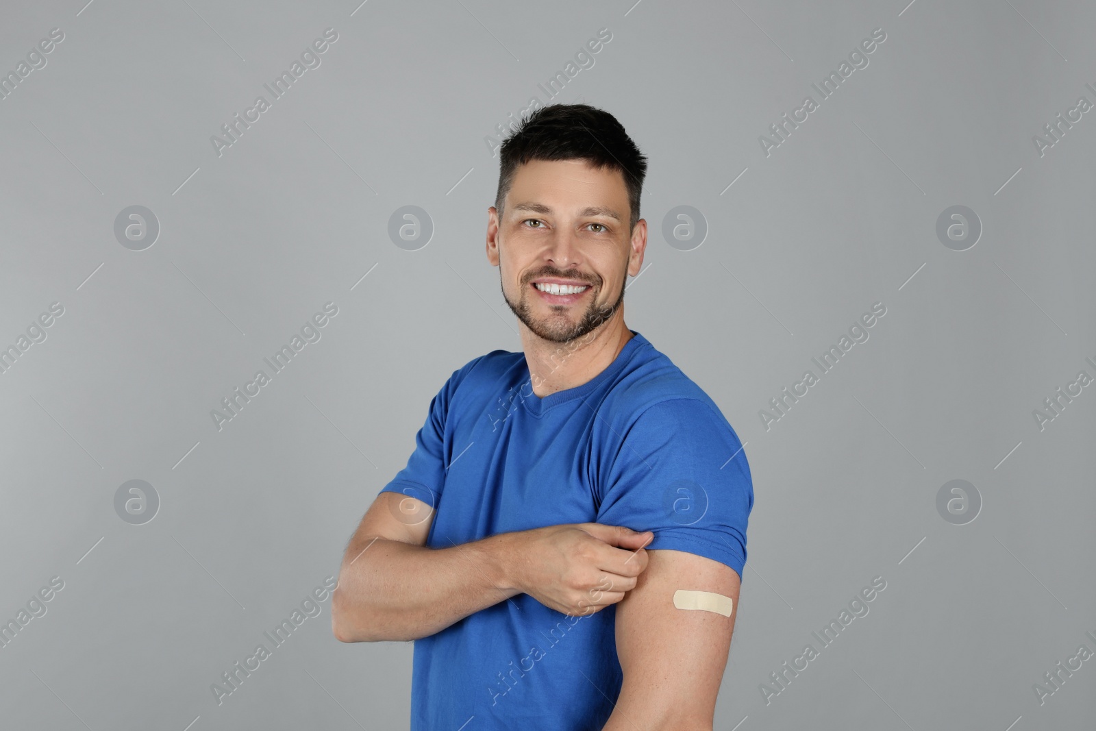 Photo of Vaccinated man with medical plaster on his arm against grey background