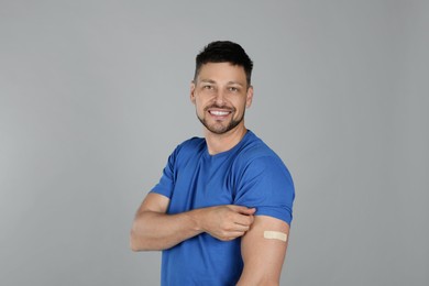 Photo of Vaccinated man with medical plaster on his arm against grey background