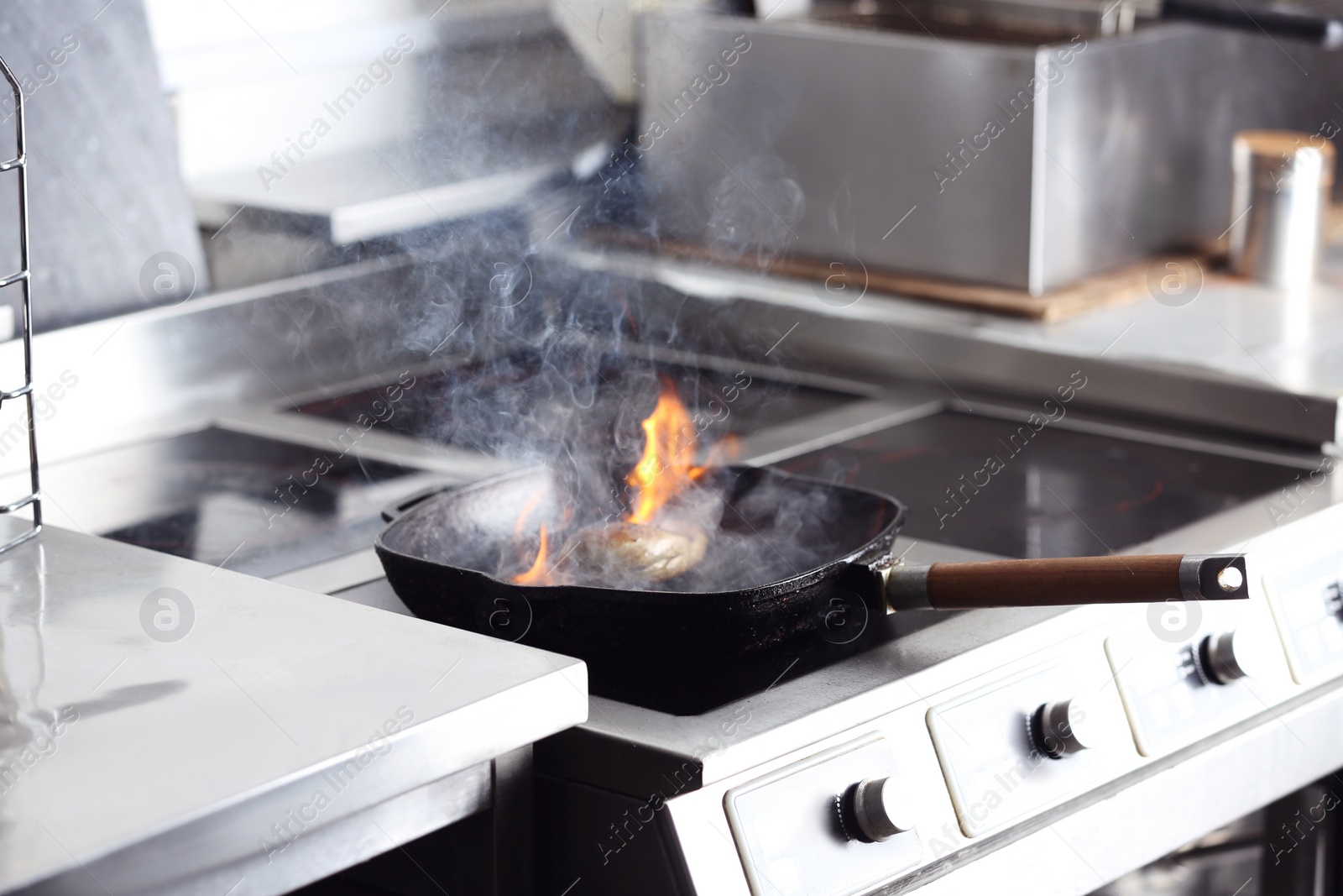 Photo of Cooking meat with burning flame in restaurant kitchen
