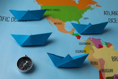 Photo of Bright paper boats and compass on world map, above view