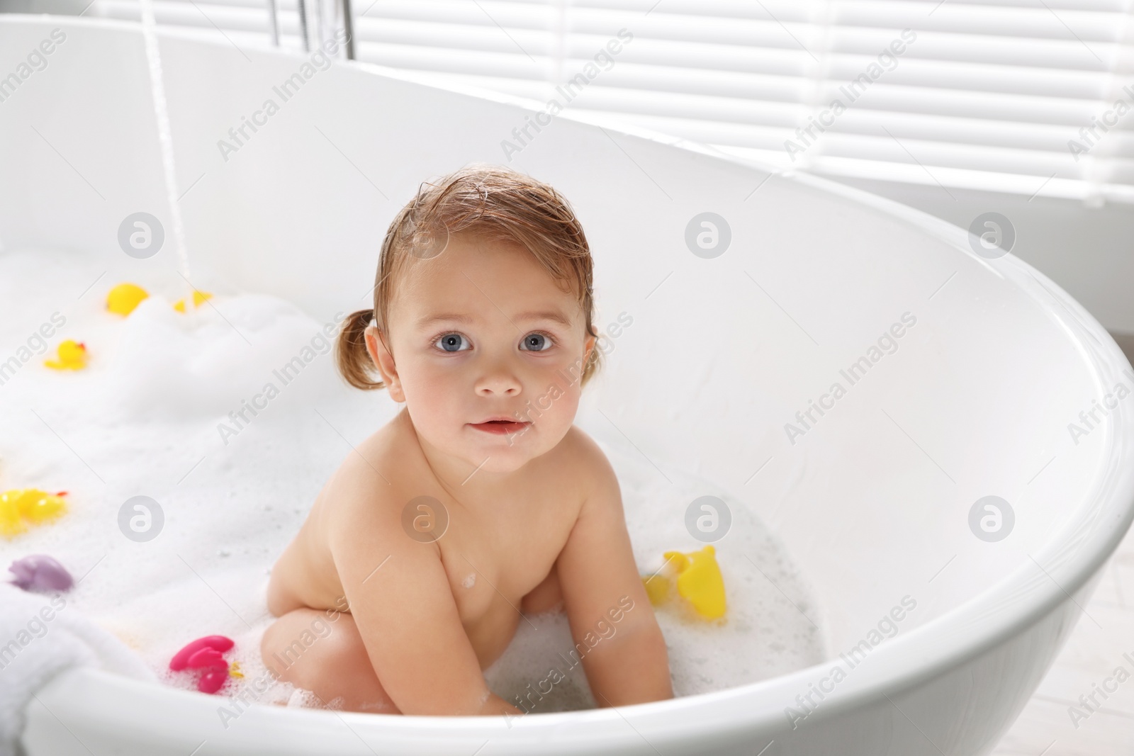 Photo of Cute little girl taking bubble bath with toys indoors