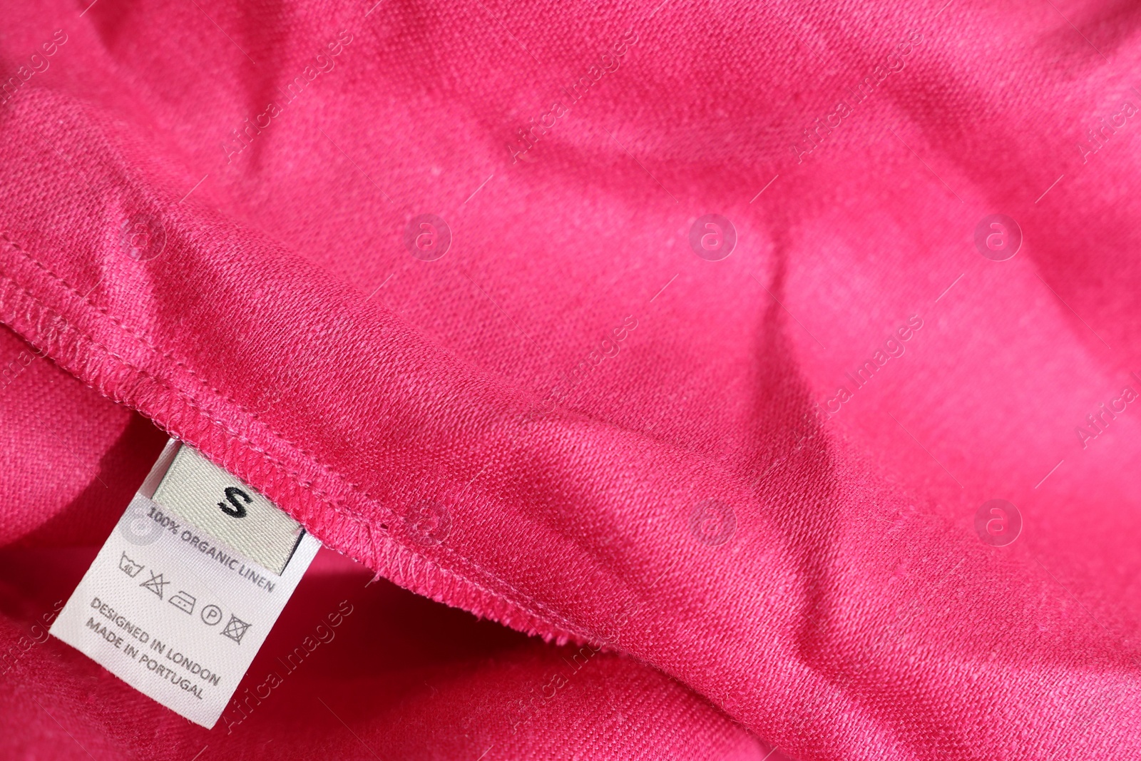 Photo of Clothing label in different languages on pink garment, closeup