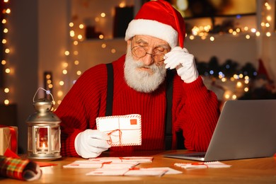 Santa Claus reading letter at his workplace in room decorated for Christmas