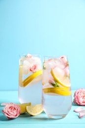 Photo of Tasty refreshing lemon drink with roses on wooden table against light blue background