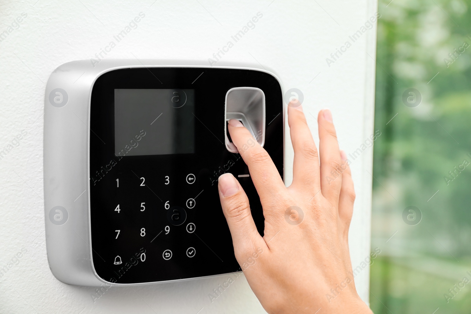 Photo of Young woman scanning fingerprint on alarm system indoors