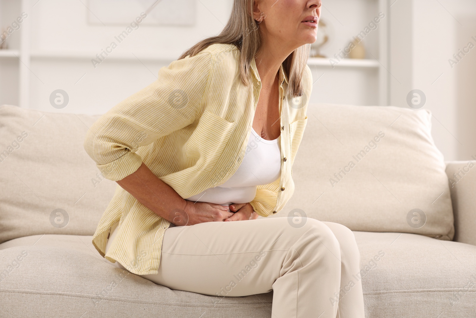 Photo of Menopause. Woman suffering from abdominal pain on sofa at home, closeup