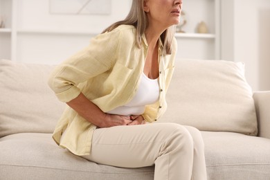 Photo of Menopause. Woman suffering from abdominal pain on sofa at home, closeup