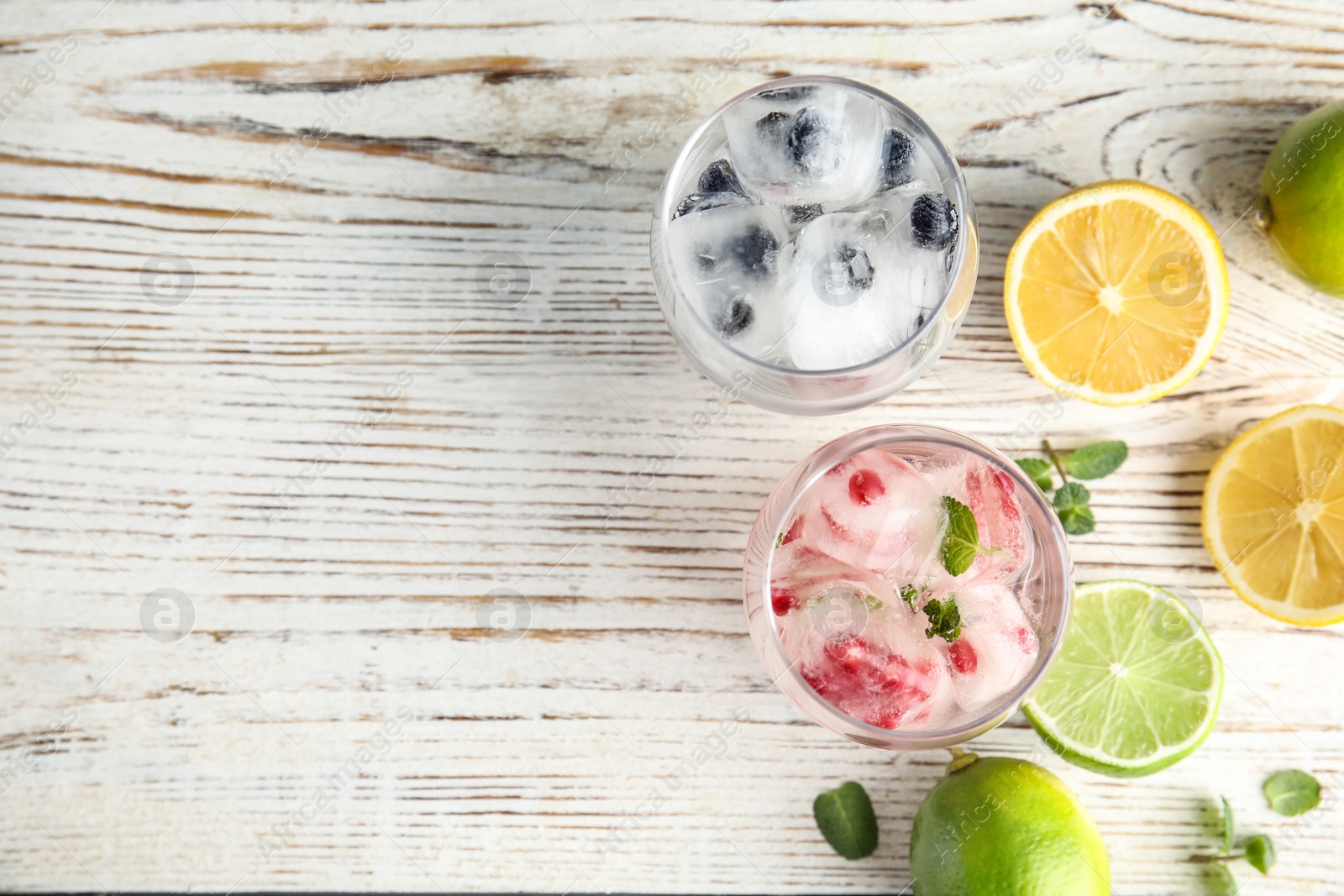 Photo of Glasses of drinks with ice cubes and fruits on wooden background, flat lay. Space for text