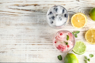 Glasses of drinks with ice cubes and fruits on wooden background, flat lay. Space for text