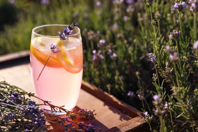 Photo of Glass of fresh lemonade on wooden tray in lavender field