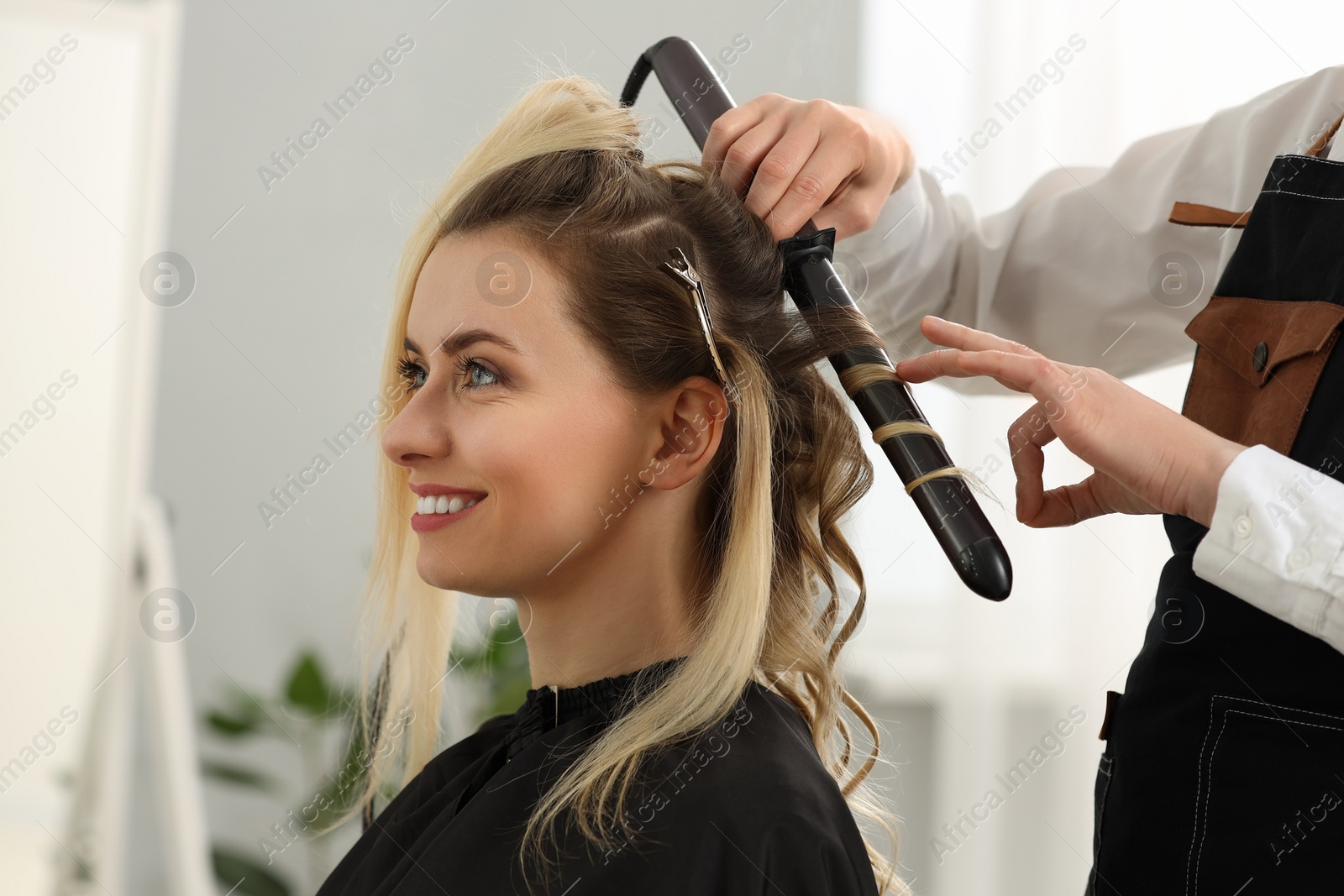 Photo of Hair styling. Hairdresser curling woman's hair in salon, closeup