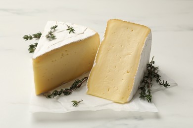 Photo of Pieces of tasty camembert cheese and thyme on white table, closeup