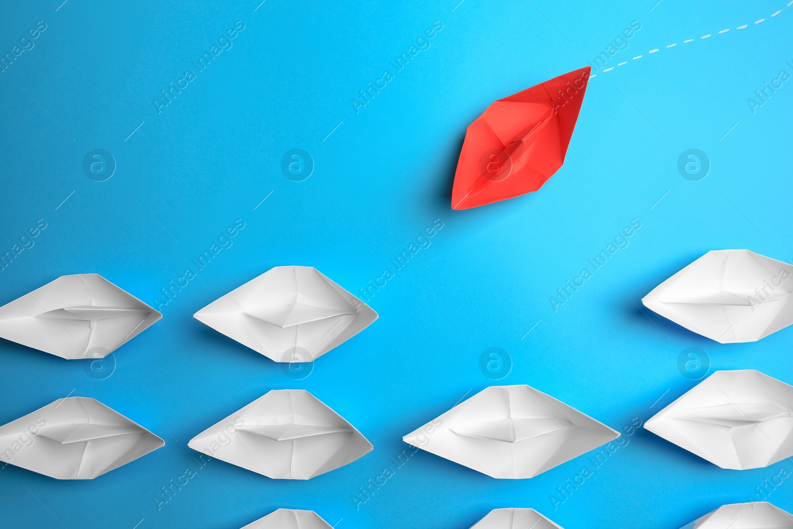 Photo of Red paper boat floating to others on light blue background, flat lay. Uniqueness concept