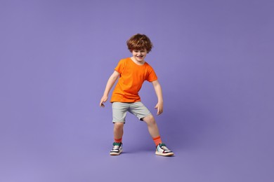 Photo of Happy little boy dancing on violet background