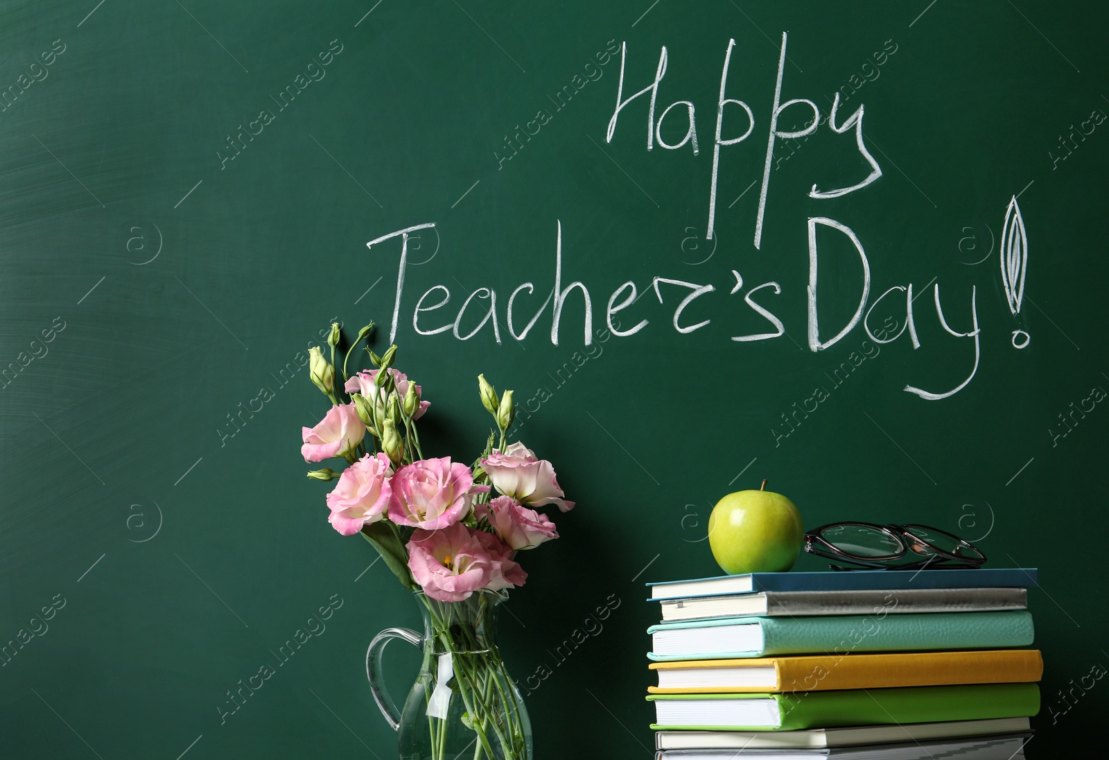 Photo of Vase of flowers and books near green chalkboard with inscription HAPPY TEACHER'S DAY