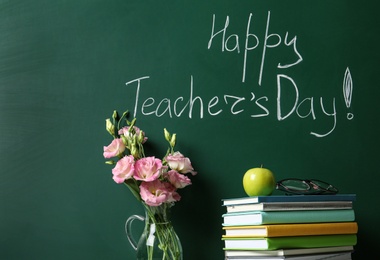 Photo of Vase of flowers and books near green chalkboard with inscription HAPPY TEACHER'S DAY