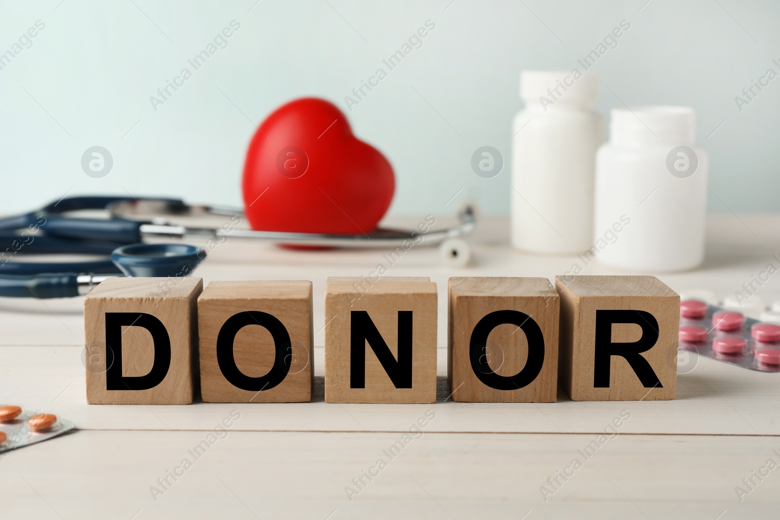 Photo of Word Donor made of cubes, red heart, stethoscope and pills on white wooden table